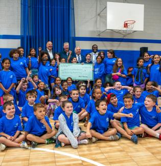 Governor McKee presenting a grant while in front of many children inside a school basketball court